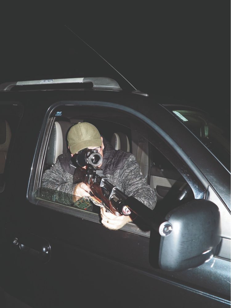 A man shooting an air rifle out of the window of a car using a thermal scope